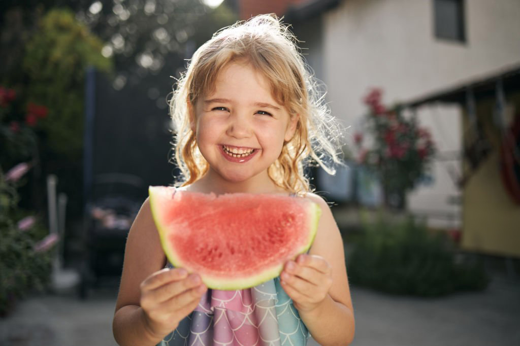 Petite fille mangeant une tranche de pastèque avec un grand sourire | Le Petit Décante